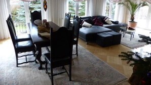 En stue med en mørk sofa, et spisebord med stole og en lysekrone.