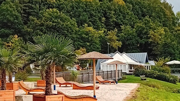 Un complexe hôtelier en bord de mer, avec des chaises longues en bois, un palmier et un kiosque.