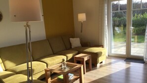 A living room with a sectional sofa, two wooden side tables, and floor lamps. - Schönes Ferienhaus in Brochterbeck mit Garten by Interhome (Tecklenburg)