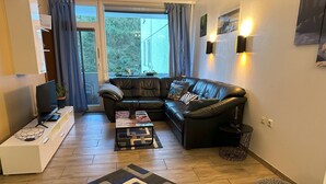 Una sala de estar moderna con un sofá de cuero, una mesa de centro, un televisor sobre un mueble bajo y una alfombra estampada.