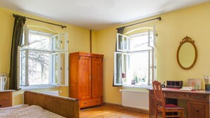 A bedroom with a wooden bed, a wooden desk with a chair, and two open windows with curtains.