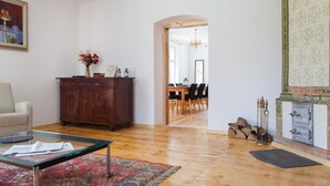 A spacious living room with a wooden floor, a glass coffee table, a sofa, a cabinet with decorative items, and a dining area in the background.