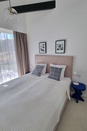 Una habitación de hotel moderna con una cama grande, dos almohadas, una mesita de noche y una ventana con cortinas.