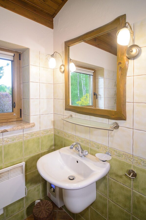 Un baño con un lavabo blanco, un espejo con iluminación y una ventana, con paredes de azulejos verdes.