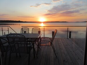 A wooden deck with metal chairs and a table overlooking a calm lake at sunset. - Seehaus Maria am See by Interhome (Mücheln)