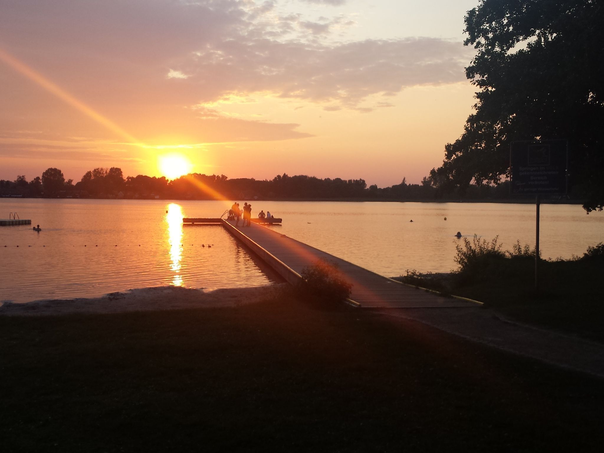 A sunset over a calm lake with a dock extending into the water.