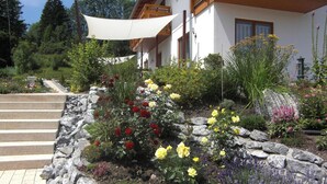 Ein Garten mit verschiedenen Blumen und Pflanzen, einem Kiesweg und einem Gebäude mit einem hölzernen Balkon.