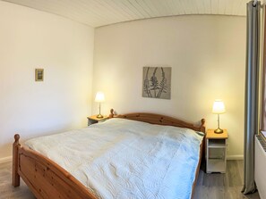 A bedroom with a wooden bed, two bedside tables with lamps, a wall-mounted artwork, and a radiator. - Landhaus by Interhome (Thomasburg)