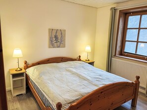 A bedroom with a wooden bed, two bedside tables with lamps, a radiator, and a window with curtains. - Landhaus by Interhome (Thomasburg)