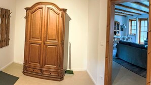 Un pasillo con un armario de madera grande, una escoba verde y una puerta que da a un salón con sofá y mesa.