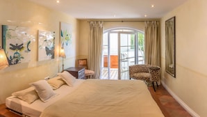 Ein geräumiges Schlafzimmer mit einem großen Bett, einem Sessel, einem Schreibtisch und Blick auf den Balkon.