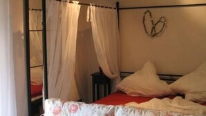 Ett sovrum med en himmelssäng, ett blommigt sängöverkast och en hjärtformad väggdekoration.