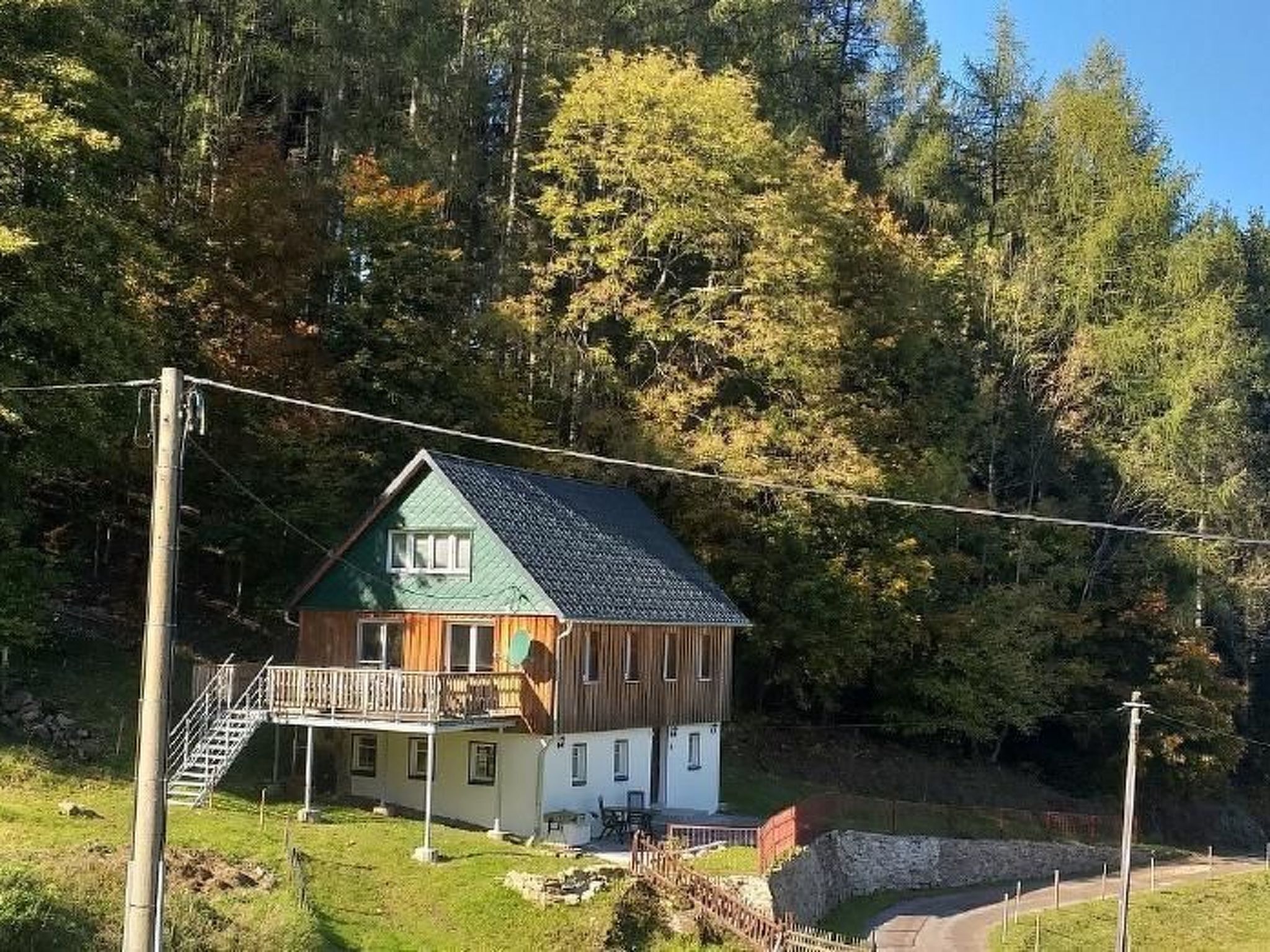En tvåvånings timmerstuga med ett grönt tak, en balkong och en liten veranda.