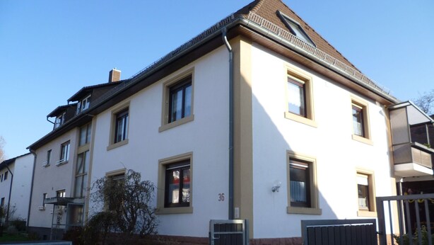 Een woongebouw met twee verdiepingen, een beige gevel, meerdere ramen en een hekwerk.