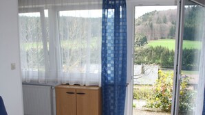 Una sala moderna con una mesa de centro de vidrio, un sofá azul y vista a un jardín a través de amplios ventanales.