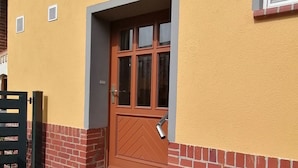 Ein Gebäude mit gelber Fassade, einer braunen Tür und einem kleinen Topfpflanzen.