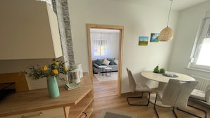 Eine moderne Küche mit Holzausstattung, ein Essbereich mit rundem Tisch und Stühlen sowie ein Wohnzimmer mit Sofa und Couchtisch.