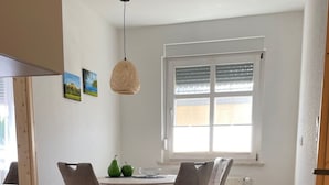 Eine moderne Küche mit Essbereich, ausgestattet mit einer Holzarbeitsplatte, einem Esstisch mit Stühlen, einer Hängeleuchte und einem Fenster mit Jalousien.