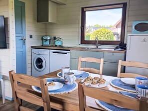 Een compacte keuken met een wasmachine, een koffiezetapparaat en een raam met uitzicht op groen.