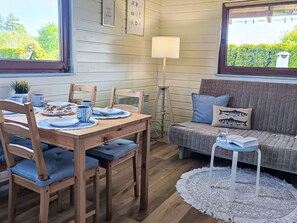 A cozy room with a dining table set for four, a sofa with cushions, a lamp, and a view of greenery outside. - Modernes Ferienhaus in Biebrowo mit Grill, Garten und Terrasse by Interhome (Choczewo)