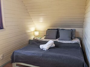 A single bed with a dark gray blanket, a white towel, and two pillows in a room with wooden paneling and a small bedside table with a lamp. - Modernes Ferienhaus in Biebrowo mit Grill, Garten und Terrasse by Interhome (Choczewo)