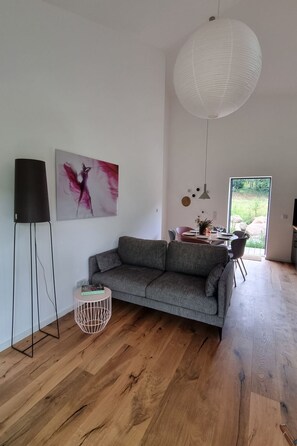 Ein modernes Wohnzimmer mit einem grauen Sofa, einer weißen Pendelleuchte und einem Bild an der Wand.