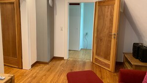 Ein Zimmer mit Holzboden, einem roten Ottomanen, einer Holztür und einem kleinen Tisch mit einer Fernbedienung.