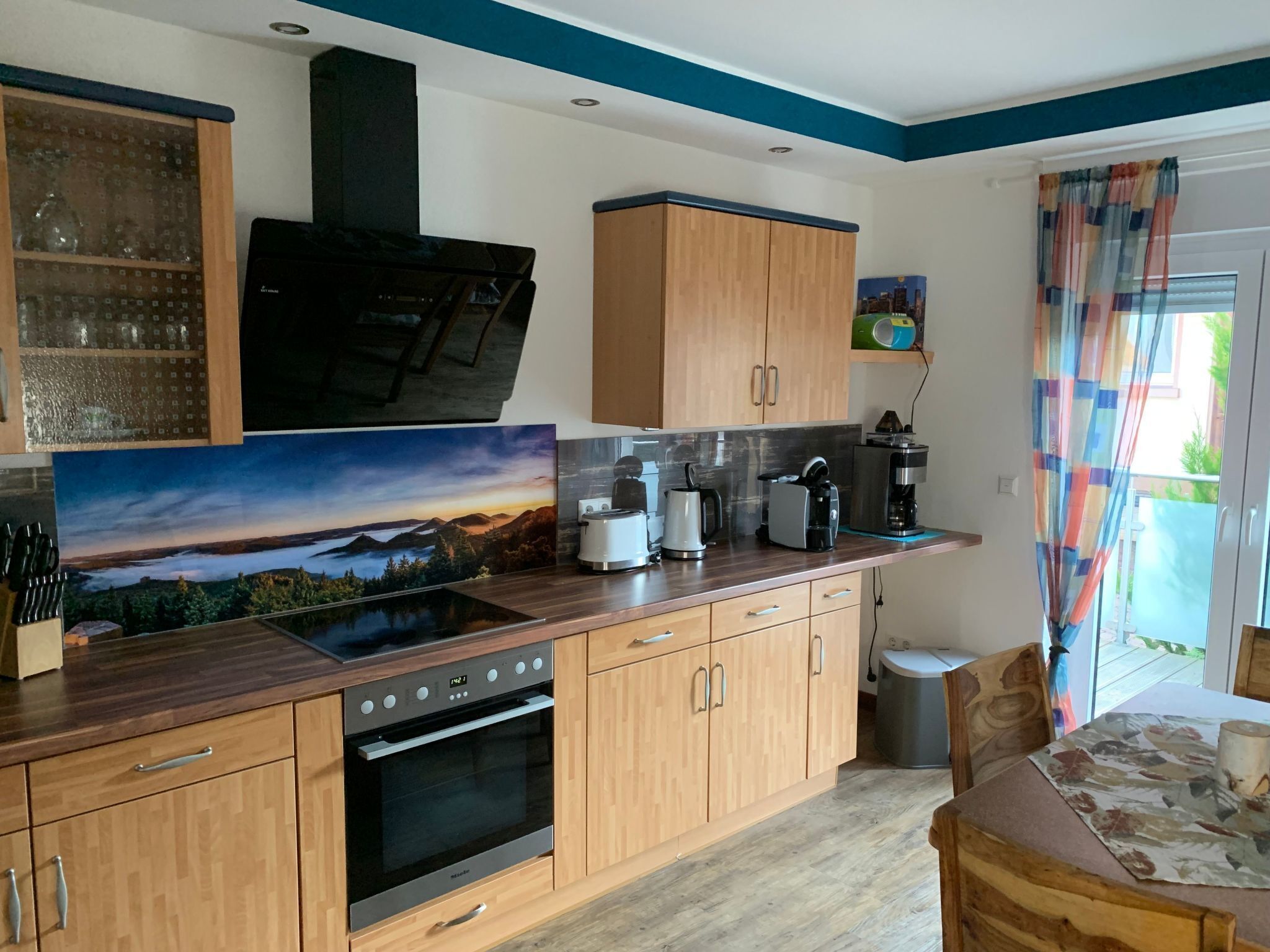 Een moderne keuken met houten kastjes, een ingebouwde oven, een koffiezetapparaat en een groot raam met uitzicht op de omgeving.