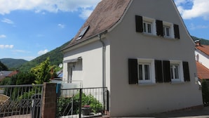 Ein zweistöckiges Haus mit einem steilen Satteldach, weißen Außenwänden und schwarzen Fensterläden.