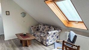 Una habitación con techo inclinado, tragaluz, sofá floral, mesa de madera y radiador.