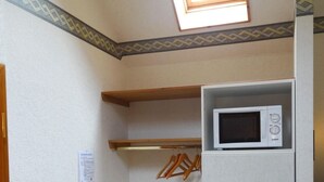 Una cocina pequeña y funcional con microondas, estantes de madera y un tendedero.