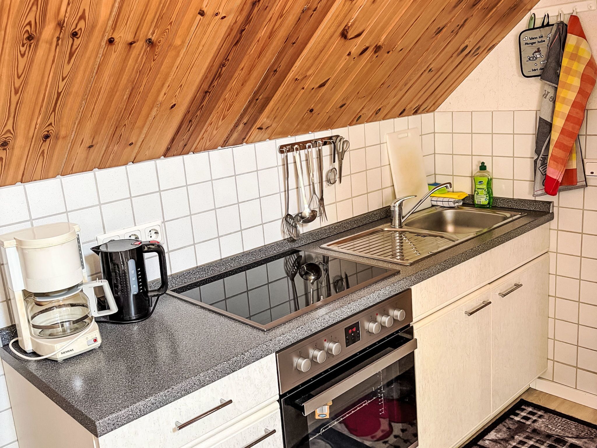 Eine Küche mit schwarzer Arbeitsplatte, weißen Schränken, einer Spüle aus Edelstahl, einer Kaffeemaschine und einem Wasserkocher.