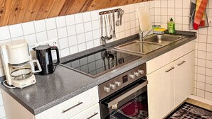 Una cocina con encimera negra, armarios blancos, pileta de acero inoxidable, cafetera y hervidor.