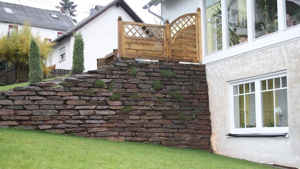 A stone wall with a wooden gate leading to a house with a white exterior and a window with a white frame. - Trappen by Interhome (Birresborn)