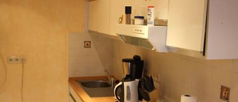 A compact kitchen with a wooden countertop, a built-in oven, a coffee maker, and a kettle.