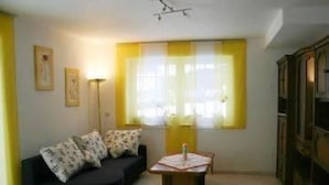 A living room with a black sofa, a small table, and a window with yellow curtains. - Trappen by Interhome (Birresborn)