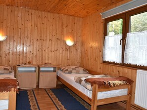 Een houten kamer met twee bedden, een klein bureau en een raam met kantgordijnen.