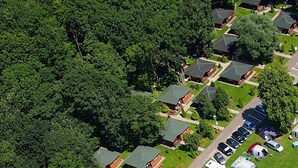 Oversigtsbillede af et boligområde med flere huse, en parkeringsplads og en tæt skov omkring ejendommene.