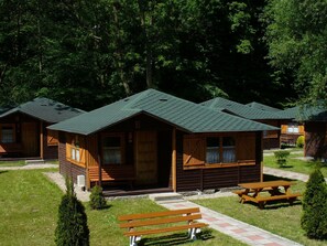 Een rij houten huisjes met groene daken, elk met een veranda en een picknicktafel.