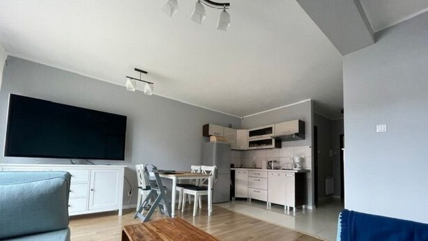 Ein modernes Wohnzimmer mit Couchtisch aus Holz, einem blauen Sofa und einem Essbereich mit weißem Tisch und Stühlen.