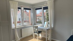 Ein Zimmer mit Holzboden, Schreibtisch und Stuhl sowie einem Fenster mit Vorhängen.