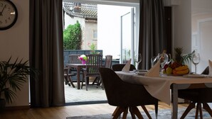 Uma sala de jantar com uma mesa posta para dois, um relógio na parede e vista para a varanda.