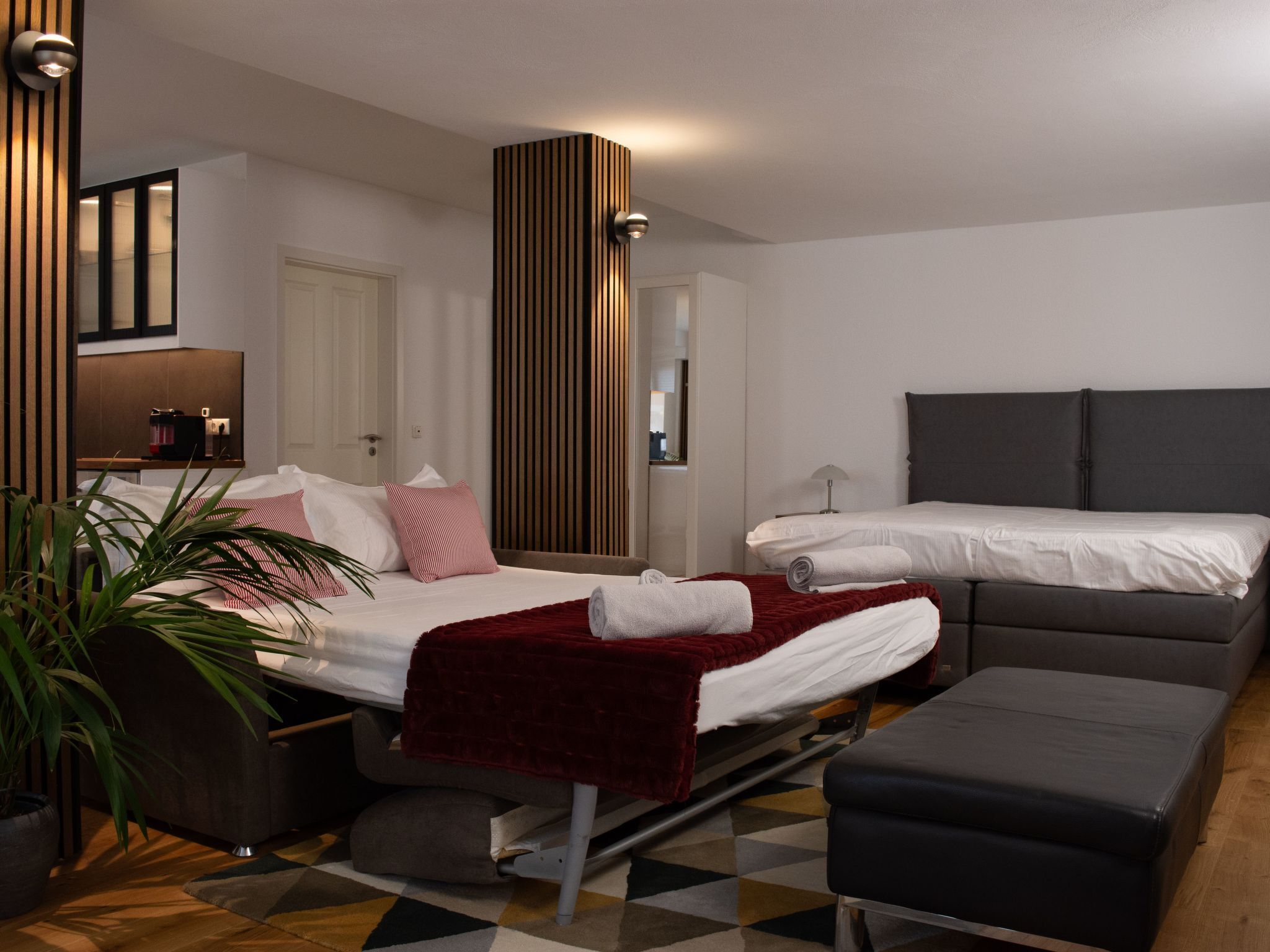 A modern hotel room with a bed, a sofa, a desk, and a potted plant.