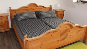 A wooden bed with a houndstooth pattern bedspread and matching pillows, flanked by wooden nightstands with lamps, in a room with a sloped ceiling and a green rug.