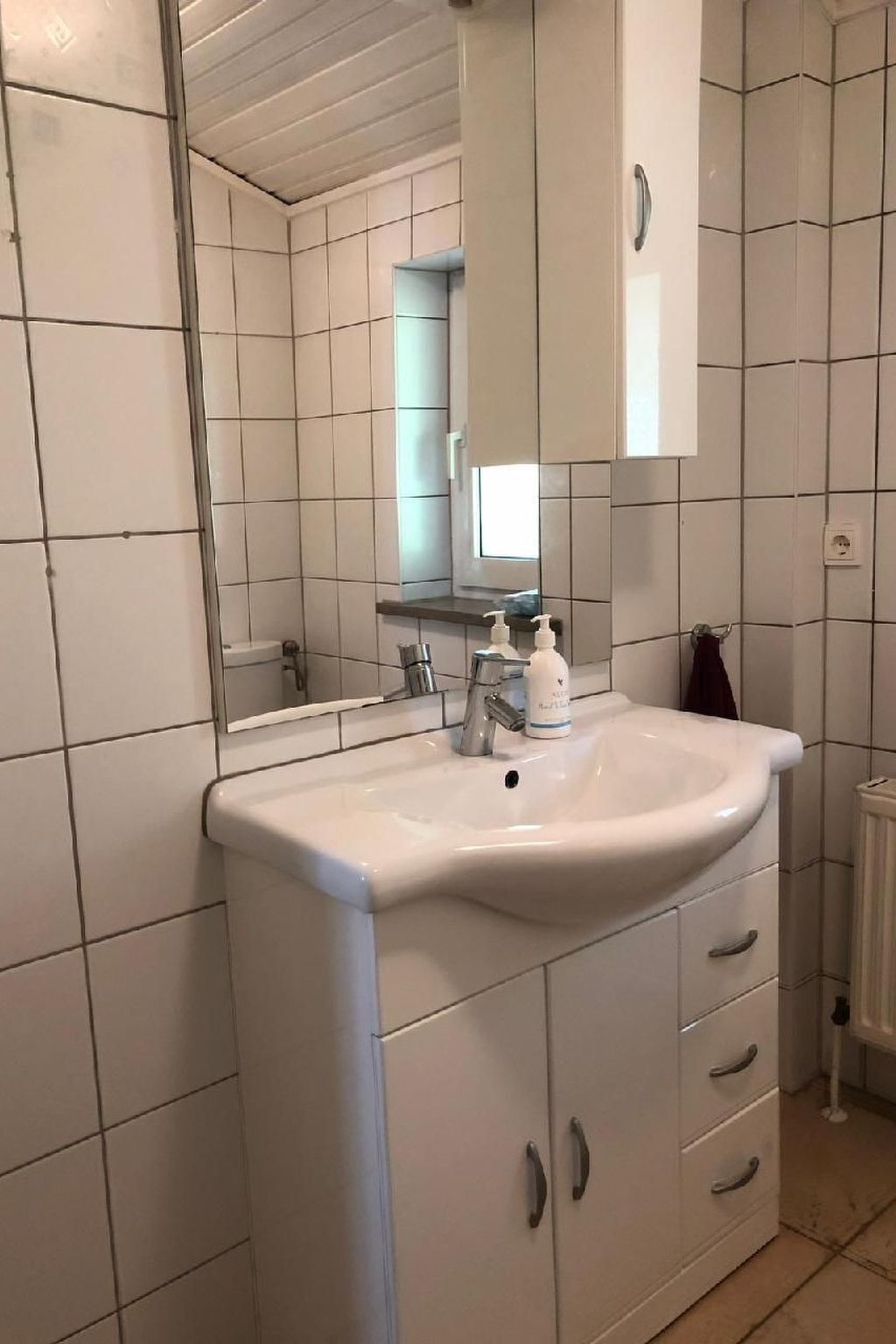 Een badkamer met een witte wastafel, spiegel en kast.