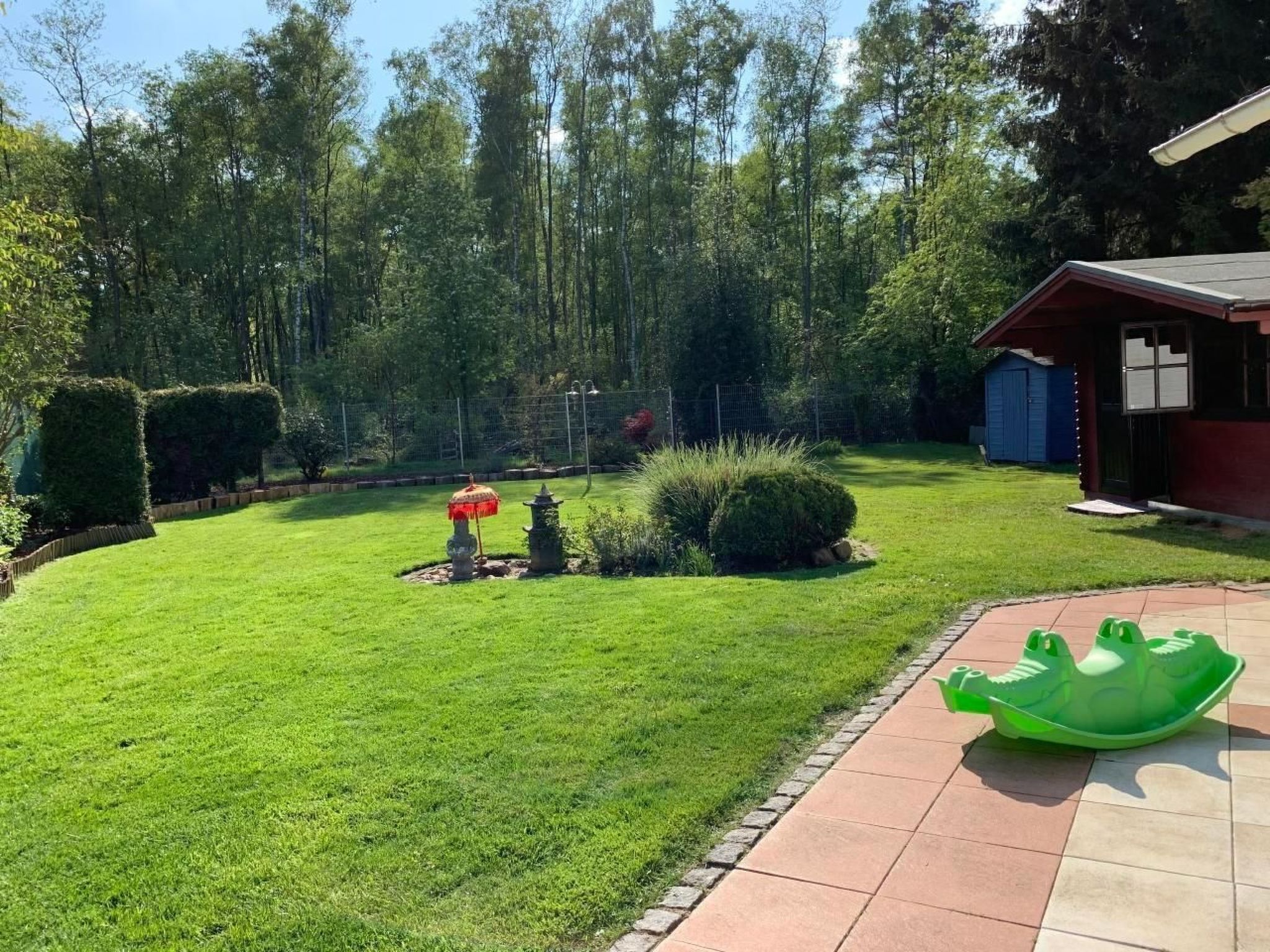 A well-maintained backyard with a lawn, a small garden area with a decorative umbrella, and a shed.