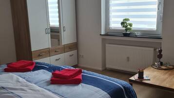 Un dormitorio con cama, armario, escritorio con planta y ventana con persianas.