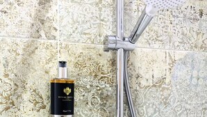 Een douche met een handdouche en een fles Vittore De' Gori The First Collection op een glazen plank.