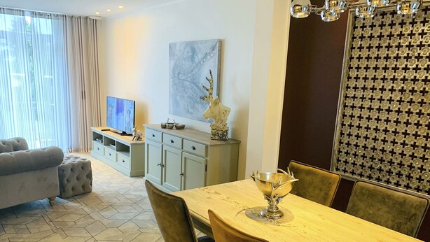 Een moderne woonkamer met een eethoek, voorzien van een bank, televisie en een decoratief wandobject.