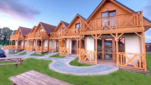 Una fila de cabañas de madera con balcones, dispuestas en línea con un sendero pavimentado en el medio.
